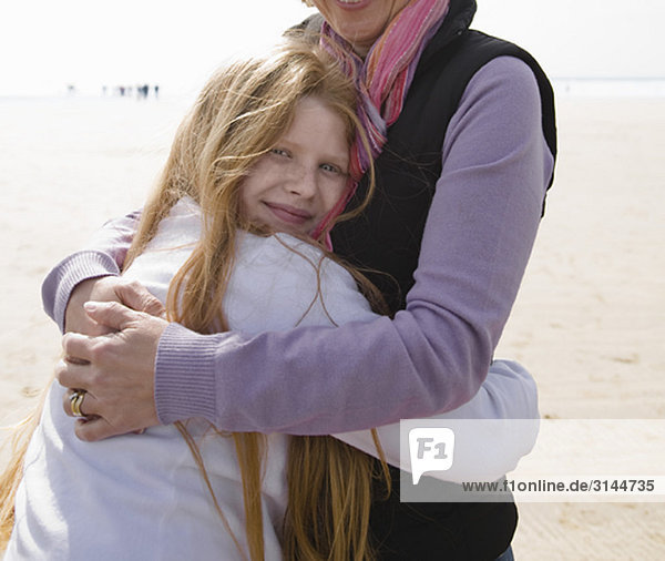 Frau umarmt Mädchen am Strand