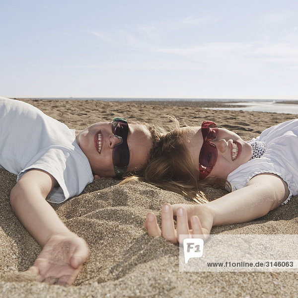 Kinder mit Sonnenbrille auf Sand liegend
