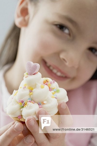 Kleines Mädchen hält Cupcake mit Sahne und Zuckerkonfetti