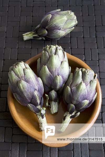 Four baby artichokes with terracotta dish
