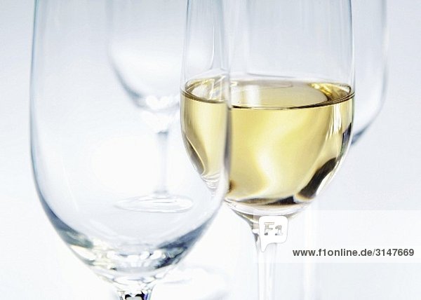 Zwei leere Gläser und ein eingeschenktes Glas Weisswein