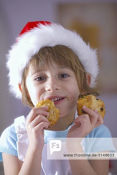 Kleines Mädchen mit Nikolausmütze isst Rosinenkekse