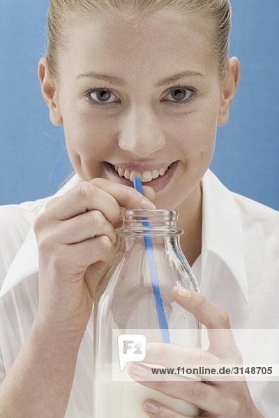 Young woman drinking milk from the bottle with a straw