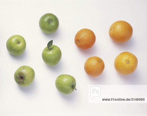 Fünf grüne Äpfel & vier Apfelsinen vor weissem Hintergrund