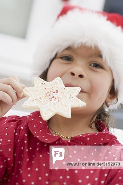 Kleines Mädchen mit Nikolausmütze hält Weihnachtsplätzchen