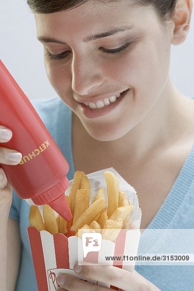 Junge Frau drückt Ketchup aus Flasche auf Pommes frites