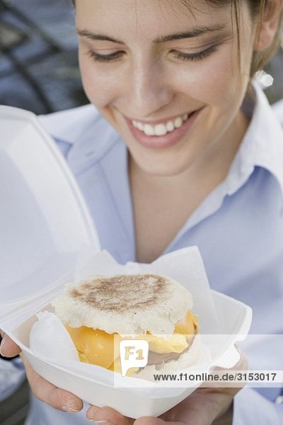 Junge Frau hält English Muffin mit Käse  Rührei und Bacon