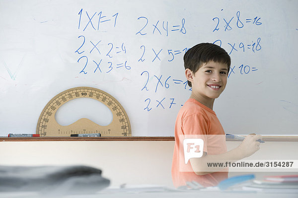 Grundschüler schreibt Gleichungen auf Whiteboard  lächelt über die Schulter vor der Kamera