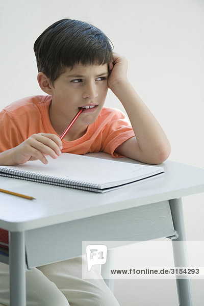 Grundschüler sitzt am Schreibtisch  stützt sich auf den Ellenbogen  kaut Bleistiftende