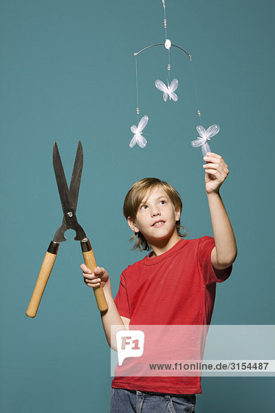 Junge mit Heckenschere schaut auf Schmetterlingsmobil