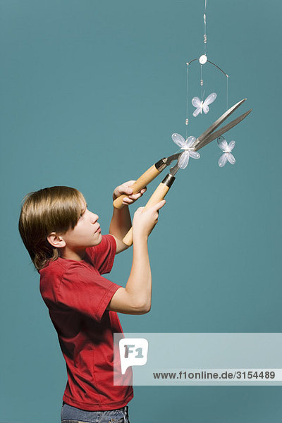 Junge benutzt Heckenschere  um Schmetterlingsmobile abzuschneiden