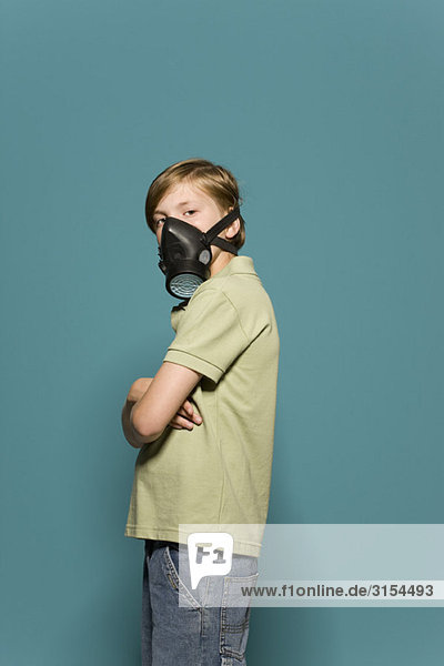 Junge mit Gasmaske  Arme gefaltet  Blick über die Schulter zur Kamera