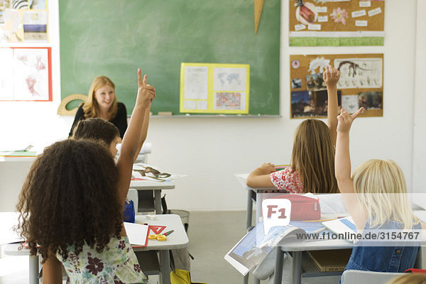 Grundschüler im Klassenzimmer mit erhobenen Händen  Rückansicht