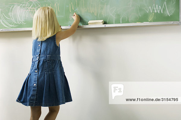 Kleines Mädchen kritzelt mit Kreide auf Tafel