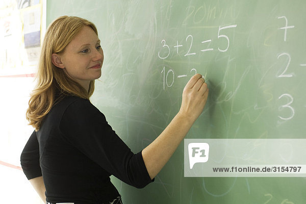 Elementary teacher writing math equations on blackboard