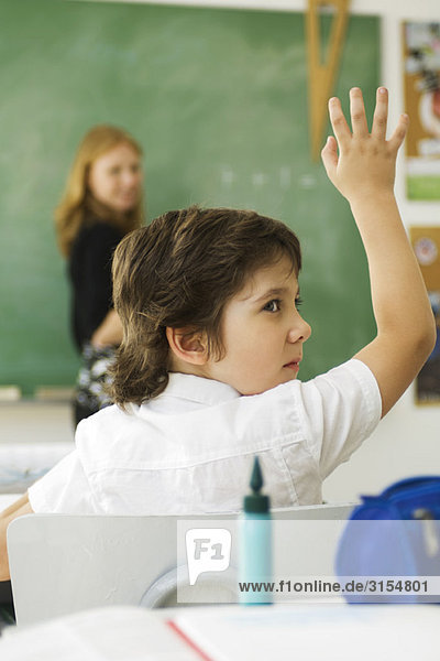 Boy raising hand in class  looking over shoulder