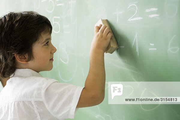 Little boy erasing classroom blackboard