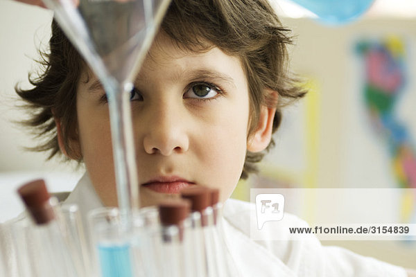 Boy pouring liquid into test tube using funnel