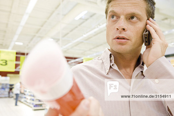 Man in supermarket using cell phone  choosing bottle of shower gel