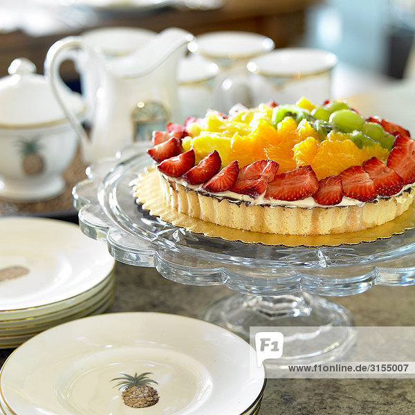 Fruit flan on glass pedestal with tea set in the background