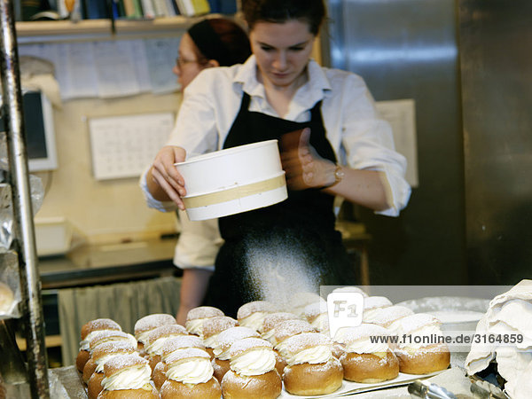A woman sifting icing sugar on cream bun with almond paste  Sweden.