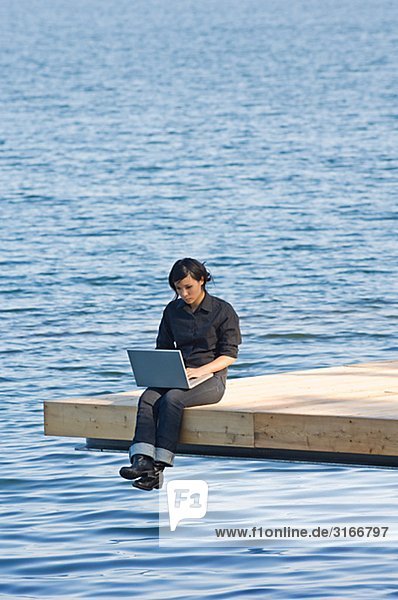 Junge Frau auf einer Mole mit einem Laptop Schweden.