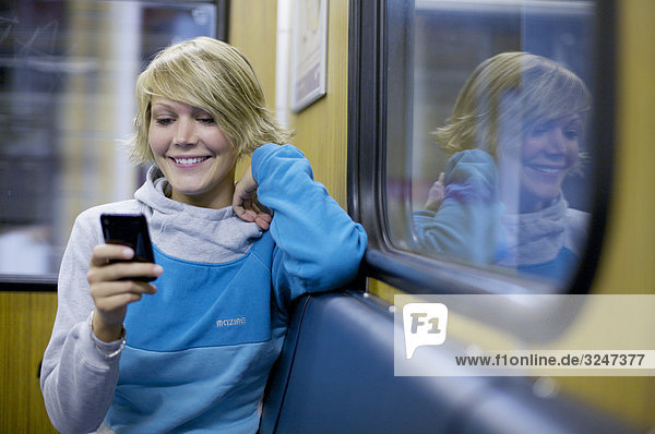 Junge Frau in S-Bahn sitzend und Mobiltelefon benutzend  Frontalansicht