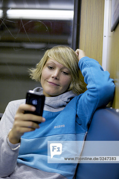 Junge Frau in S-Bahn sitzend und Mobiltelefon benutzend  Frontalansicht