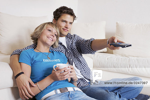 Teenager couple sitting in front of couch and watching television  horizontal format