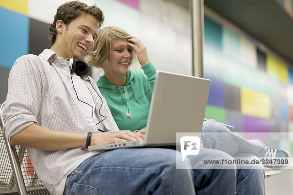 Teenager couple using laptop at underground station  low-angle view