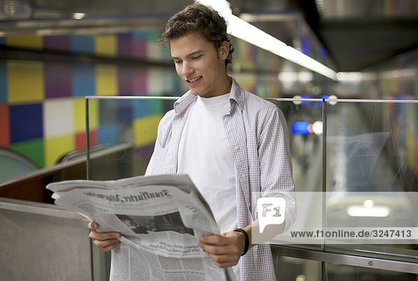 Young man reading newspaper in underground station  waist up