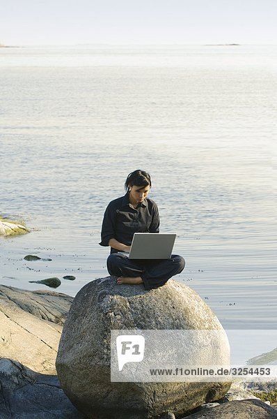 Junge Frau mit einem Laptop am Meer  Schweden.