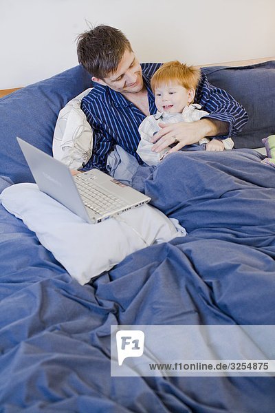 A father and son using a laptop in bed  Sweden.