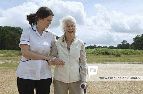 Ältere Frau wird von einer Krankenschwester unterstützt.