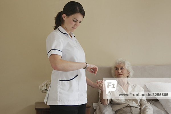 Krankenschwester  die den Puls einer älteren Frau nimmt