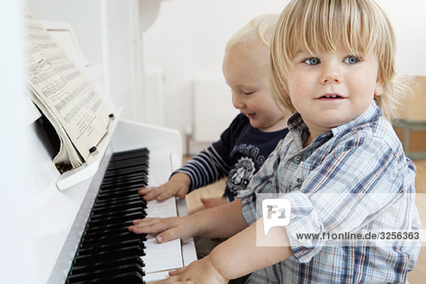 Two boy toddlers sitting at a piano