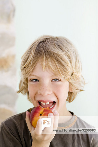 Ein Junge  der eine Nektarine isst.