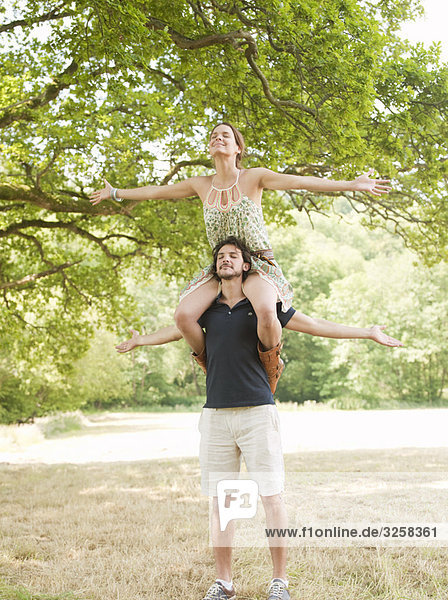 woman on mans shoulders under tree