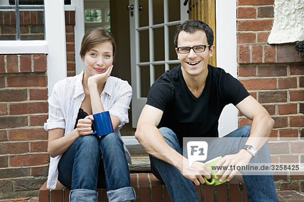 Ein junges Paar  das auf der Türschwelle sitzt.