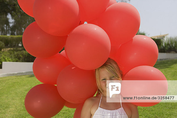 Young girl holding bunch of red balloons