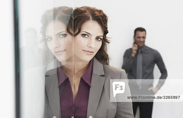 Geschäftsfrau neben der Glastür,  Mann im Hintergrund per Handy