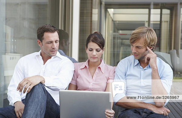 Deutschland,  Köln,  Drei Geschäftsleute sitzen Seite an Seite,  mit Laptop