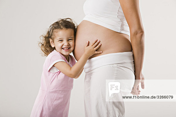 Girl (4-5) embracing mother's pregnant belly
