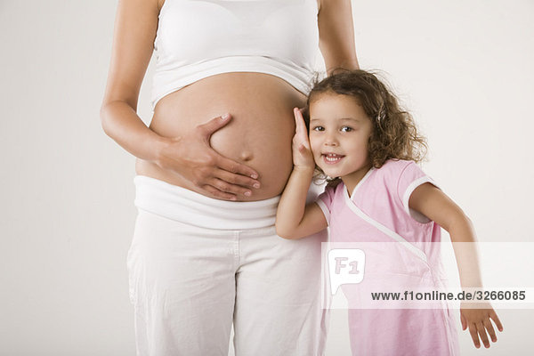 Mädchen (4-5) legt Ohr an den Bauch der schwangeren Mutter