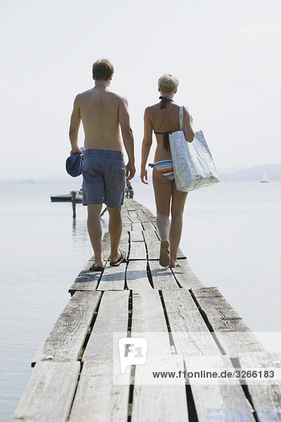 Germany  Bavaria  Young couple wearing swimwear walking on jetty  rear view