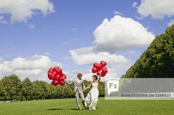 Deutschland,  Bayern,  Brautpaar mit roten Luftballons im Freien