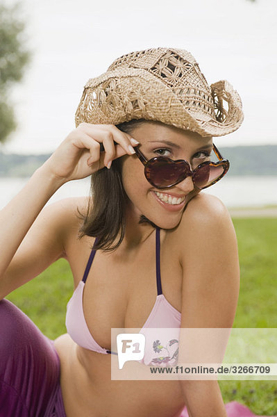 Starnberger See  Junge Frau sitzt im Park mit Sonnenbrille und Hut  lächelnd  Portrait  Nahaufnahme