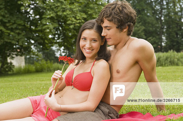 Starnberger See  Junges Paar auf Decke im Park sitzend  Frau hält Blume  lächelnd  Porträt