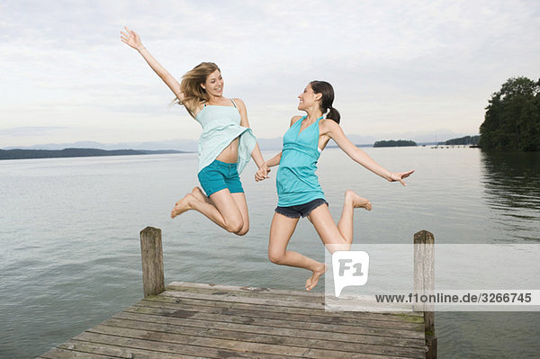 Starnberger See  Two young women jumping on jetty  laughing  portrait