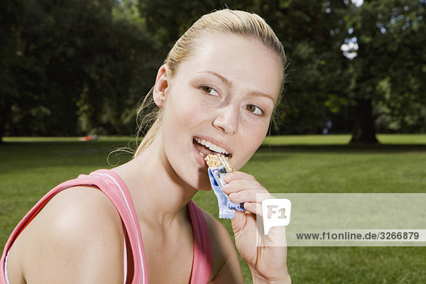 Junge Frau im Park beim Essen eines Müsli-Riegels  Porträt